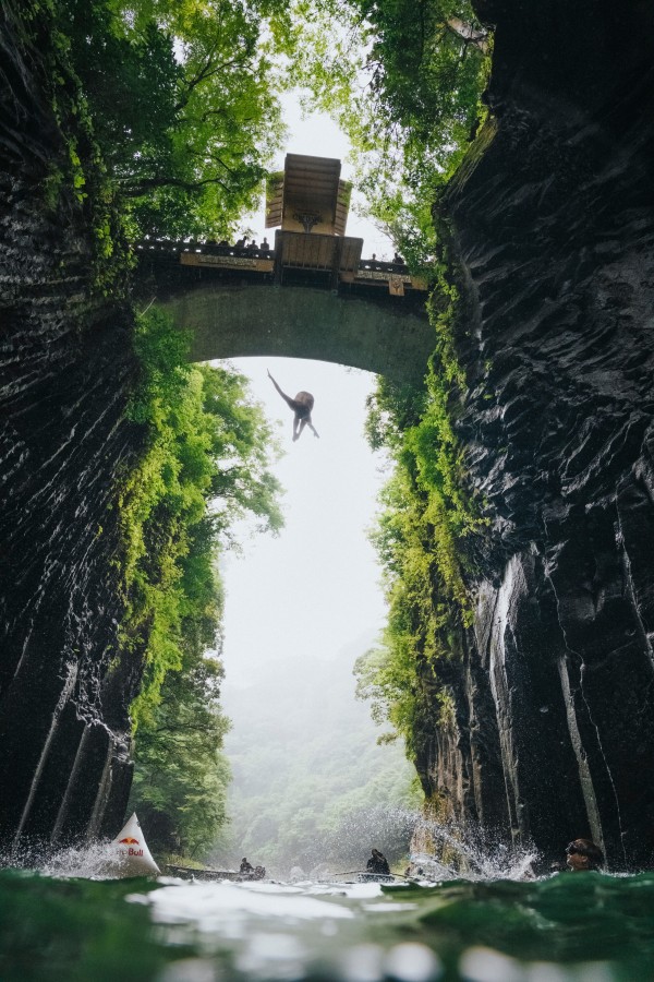 Framed between two sides of a gorge, a diver jumps from a platform spanning the gorge top.